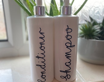 May include: Two white pump bottles with black script labels. The bottle on the left says "Conditioner" and the bottle on the right says "Shampoo".