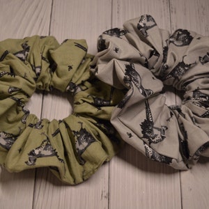 May include: Two fabric scrunchies with a black and white print of a bird. One scrunchie is green and the other is gray.