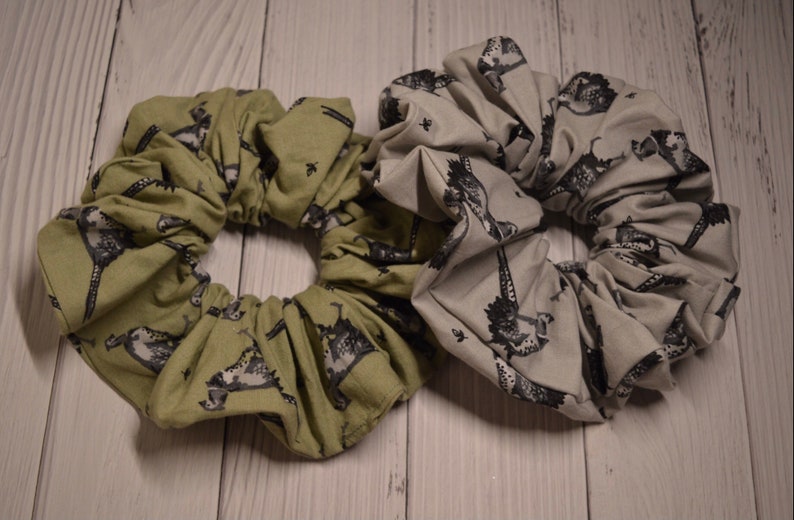 May include: Two fabric scrunchies with a black and white print of a bird. One scrunchie is green and the other is gray.