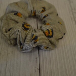 May include: A beige fabric scrunchie with a pattern of small yellow and black bees.
