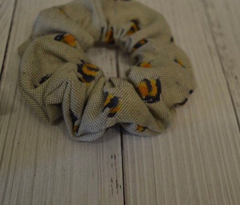 May include: A beige fabric scrunchie with a pattern of small yellow and black bees.