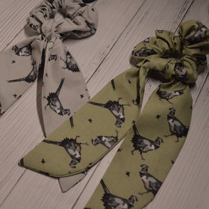 May include: Two fabric hair scrunchies with pheasant print. One is gray and the other is green.