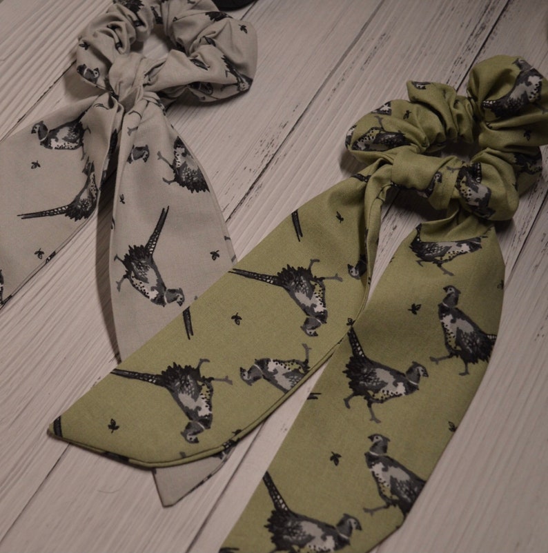 May include: Two fabric hair scrunchies with pheasant print. One is gray and the other is green.