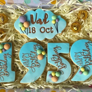 May include: A set of blue and white cookies decorated with gold lettering and colourful sprinkles. The cookies spell out "Happy Birthday" and the number "19". There is also a cookie with the name "Val" and the date "18 Oct".
