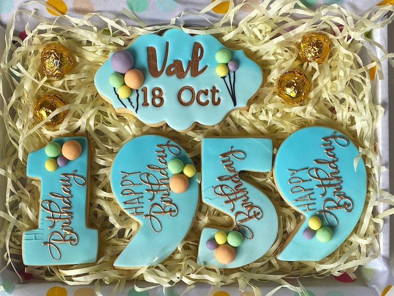 May include: A set of blue and white cookies decorated with gold lettering and colourful sprinkles. The cookies spell out "Happy Birthday" and the number "19". There is also a cookie with the name "Val" and the date "18 Oct".
