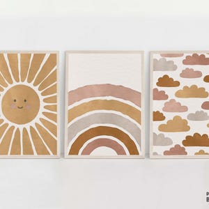 Pode incluir: Três impressões de arte de parede minimalistas com um tema boho. A primeira impressão apresenta um sol sorridente com raios em tons de marrom. A segunda impressão apresenta um arco-íris em tons de marrom, rosa e cinza. A terceira impressão apresenta um padrão de nuvens em tons de marrom, rosa e cinza.