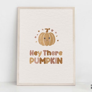 May include: A printable wall art print with a cute cartoon pumpkin with a smiling face and the text "Hey There PUMPKIN". The background is a light beige color with brown and pink accents.