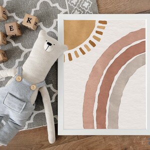 May include: A framed print with a watercolor illustration of a rainbow and sun in shades of brown, pink, and gray. The print is on a white background and has a white frame.