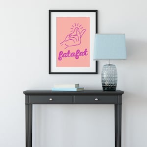 May include: A framed art print with a pink background features a hand gesture and the word "fatafat" in purple. The print hangs above a black console table with a lamp and books.