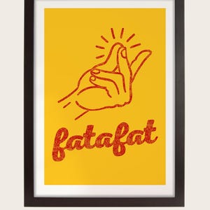 a hand gesture with the word "fatfat" written below it in a red font against a yellow background. The image is framed in a black wood frame.