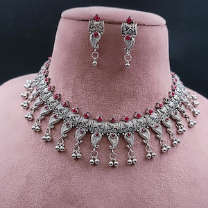 Puede incluir: Un conjunto de collar y pendientes de plata con un diseño delicado y piedras rojas. El collar presenta una fila de colgantes en forma de lágrima con pequeñas bolas de plata que cuelgan de ellos.