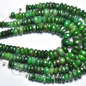 May include: Strands of faceted emerald beads in varying shades of green. The beads are strung on thin, silver-colored wire, creating a shimmering effect. The gemstones have a polished, reflective surface.