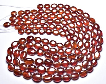 May include: A strand of reddish-brown gemstone beads, likely garnet, with a smooth, oval shape. The beads are strung on a white thread and are arranged in a circular pattern.