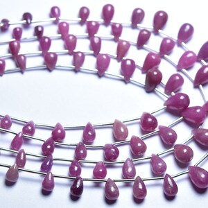 May include: A strand of pink gemstone beads in a teardrop shape. The beads are strung on silver wire and are arranged in a circular pattern.