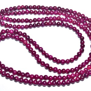 Può includere: Una collana di perle di pietra preziosa rosa intenso. Le perle sono rotonde e lisce e sono infilate su un filo sottile.