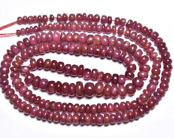 May include: A strand of ruby red gemstone beads. The beads are faceted and have a slightly irregular shape. The beads are strung on a thin red thread.