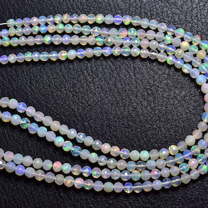 May include: A strand of white opal beads with iridescent rainbow colors. The beads are round and have a smooth, polished finish.