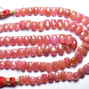 Op de afbeelding: Een streng roze edelsteen kralen met een gefacetteerde afwerking. De kralen zijn geregen op een rode draad en hebben een natuurlijke, licht onregelmatige vorm. De streng is aan beide uiteinden afgewerkt met rode kwastjes.