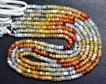 May include: A collection of faceted opal bead strands, displaying a spectrum of colours from white and yellow to orange and red. The beads are strung on white thread, creating a textured, colourful display. The beads are small and uniform in size.