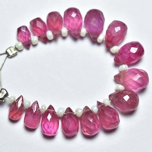 May include: A strand of pink gemstone beads with a faceted teardrop shape. The beads are separated by small white beads.
