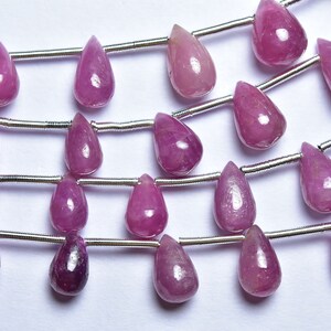 May include: A strand of pink gemstone beads in a teardrop shape. The beads are strung on a silver wire.