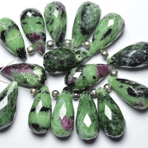 Könnte beinhalten: Eine Strähne aus 15 facettierten grünen und schwarzen Edelsteinen mit rosafarbenen Akzenten. Die Perlen sind tropfenförmig und auf silbernem Draht aufgefädelt.