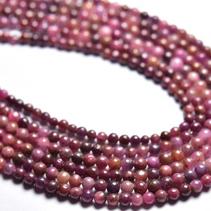 May include: A strand of pink ruby gemstone beads. The beads are round and have a smooth, polished finish. The beads are strung on a clear thread.