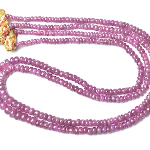 Peut inclure: Un collier à plusieurs rangs composé de petites perles rondes et facettées de couleur rouge rosé. Les rangs sont réunis à une extrémité par deux embouts coniques dorés ornés de fils rouges, maintenant les multiples rangées de perles.