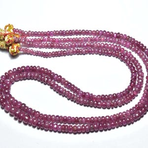 May include: A necklace of small, round, pink gemstones. The beads are strung together in multiple strands, creating a layered effect. The necklace has a decorative gold and red tassel at the top.