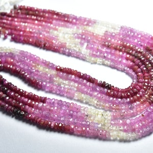 May include: A strand of pink, red, and white gemstone beads. The beads are faceted and have a slightly irregular shape. The strand is made up of multiple rows of beads.