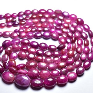 Peut inclure: Un brin de perles de rubis roses de forme ovale. Les perles sont lisses et polies, avec un léger éclat.