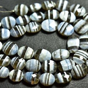 May include: A strand of oval-shaped, faceted gemstone beads. The beads are a mix of light blue and brown with white stripes. The beads are strung on a silver wire.