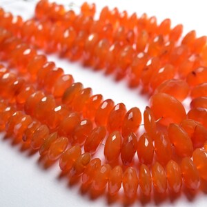 May include: A strand of orange carnelian beads, faceted and oval shaped. The beads are strung on a wire and are ready to be used for jewelry making.