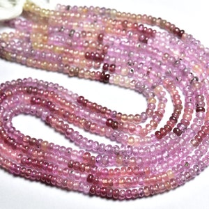 Puede incluir: Una hebra de cuentas de piedras preciosas de color rosa y rojo. Las cuentas son pequeñas y redondas, y están enhebradas en un hilo transparente. Las cuentas están dispuestas en un patrón suelto y fluido.