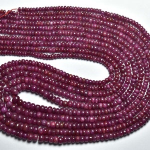 Pode incluir: Um fio de contas de cor vermelha rubi, com um acabamento liso e polido. As contas são enfiadas em um fio vermelho e estão dispostas em um padrão circular.