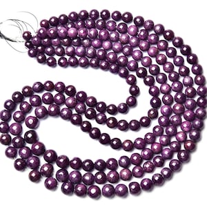 May include: A long strand of round, deep purple beads with a subtle, natural mottled texture. The beads are strung together on a thin black thread, arranged in a curved, overlapping loop pattern against a plain white background.