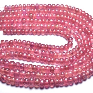 Può includere: Fili di perline di pietre preziose rosa. Le perline sono piccole, rotonde e lucide. Il colore è un rosa tenue e rosato. Le perline sono infilate, pronte per la creazione di gioielli. L'immagine è ben illuminata, mostrando i dettagli.