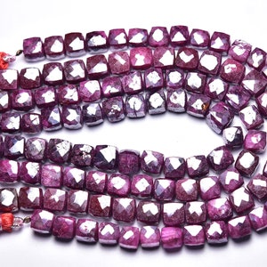 Może przedstawiać: Sznur fasetowanych koralików rubinowych w kształcie kwadratu. Koraliki są ciemnoróżowe z lekkim połyskiem. Sznur zakończony jest czerwonymi frędzlami.