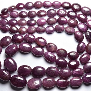 Op de afbeelding: Een streng ovale, paarse robijn kralen. De kralen zijn glad en gepolijst, met een lichte glans.