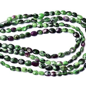 May include: Multiple strands of faceted oval beads made of green zoisite with dark purple ruby inclusions. The beads are strung on thin silver-toned wire, creating a layered arrangement of natural stone textures with varying shades of green and purple.