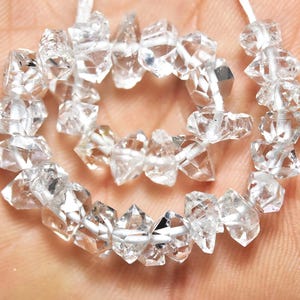 May include: A strand of clear, faceted, diamond-shaped beads. The beads are strung on a white cord and are arranged in a circular pattern.