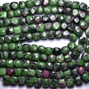 May include: A strand of green and red gemstone beads. The beads are faceted and have a square shape. The beads are strung on a thin cord.