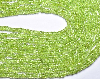 May include: A strand of light green peridot gemstone beads. The beads are faceted and have a rough, irregular shape. The beads are strung on a clear thread and are arranged in a loose, flowing pattern.