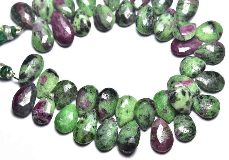 K&ouml;nnte beinhalten: Eine Str&auml;hne aus gr&uuml;nen, rosa und schwarzen Edelsteinperlen. Die Perlen sind birnenf&ouml;rmig und haben eine facettierte Oberfl&auml;che.