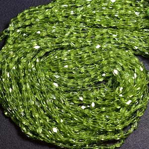 May include: A strand of green peridot beads, faceted and cut into rectangular shapes. The beads are strung together on a clear thread.