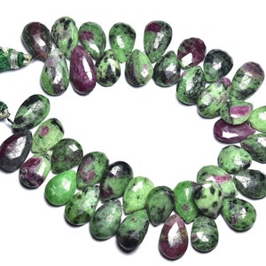 K&ouml;nnte beinhalten: Eine Kette aus gr&uuml;nen und rosafarbenen Edelsteinperlen, jede Perle ist ein birnenf&ouml;rmiger Tropfen mit einer facettierten Oberfl&auml;che. Die Perlen sind auf einer Schnur mit gr&uuml;nen Quasten an jedem Ende aufgef&auml;delt.