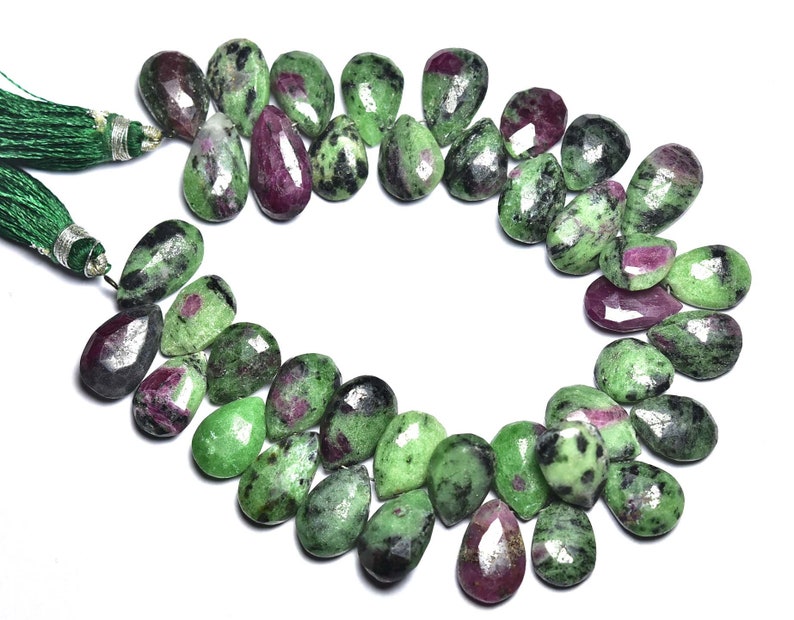 K&ouml;nnte beinhalten: Eine Kette aus gr&uuml;nen und rosafarbenen Edelsteinperlen, jede Perle ist ein birnenf&ouml;rmiger Tropfen mit einer facettierten Oberfl&auml;che. Die Perlen sind auf einer Schnur mit gr&uuml;nen Quasten an jedem Ende aufgef&auml;delt.