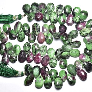 May include: A strand of green and pink gemstone beads, with a pear-shaped cut. The beads are strung on a cord with green tassels at each end.