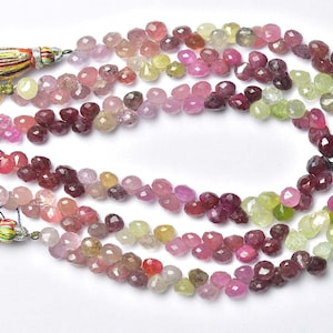 May include: Strings of faceted gemstone beads in shades of pink, purple, green, and yellow. The beads are teardrop-shaped and strung together. Tassels with colourful threads are visible at the end of the strings.