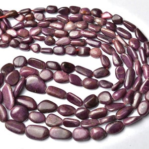 May include: A strand of purple gemstone beads, each bead is a smooth, elongated oval shape. The beads are strung on a red thread.